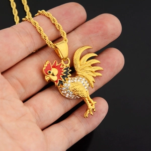 Detailed view of a golden rooster pendant with red enamel and sparkling crystal inlay