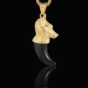 Gros plan du pendentif tête de loup dorée avec croc noir sur chaîne en or