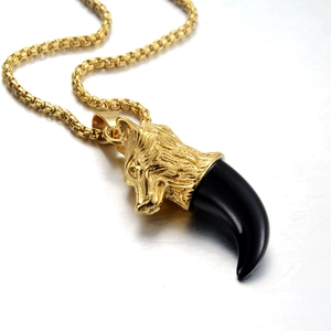 Vue macro du collier pendentif tête de loup dorée avec corne noire et chaîne à billes