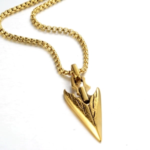 Gros plan sur le collier pendentif pointe de flèche dorée avec surface texturée vintage