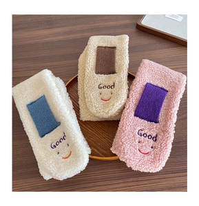 Detail von flauschigen Babysocken mit Smiley-Stickerei in einem runden Tablett