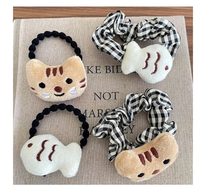 Détail de breloques chat et poisson en peluche sur des chouchous élastiques à carreaux