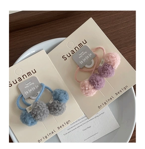 Detail of colorful plush ball hair ties in pink, purple and blue on white display plate