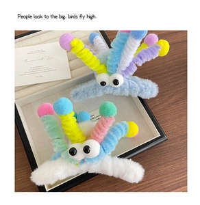 Détail de pinces à cheveux monstre en peluche avec antennes colorées dans une boîte cadeau