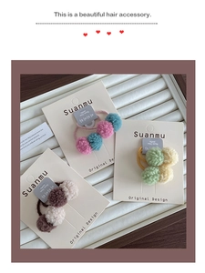 Close-up of three colorful plush ball elastic hair ties displayed on a white jewelry tray
