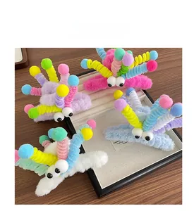 Détail d'une pince à cheveux peluche avec de grands yeux et des pompons colorés