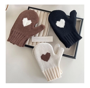 Three pairs of knitted kids' mittens in black, brown, and cream with heart patterns