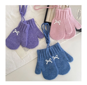 Flat lay of colorful knit toddler mittens with white bow accents and neck strings