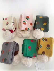 Dettagli dei motivi floreali in maglia e pompon bianchi su morbide sciarpe invernali da bimbi