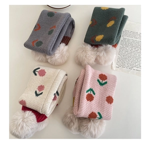 Dettaglio della trama a maglia di sciarpe per bambini con motivi floreali e pompon morbidi