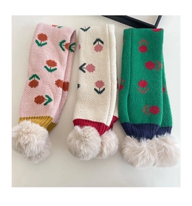Dettaglio di sciarpe floreali a maglia con morbidi pompon in rosa, crema e verde delicato