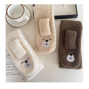 Close-up of plush lamb wool scarves with cute bear embroidery in warm white and brown tones
