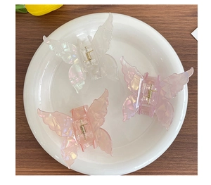 Détail de trois pinces à cheveux papillon irisées en blanc rose et lilas sur un plat