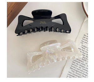 Top view of large acetate bow hair claws in glossy black and pearly cream colors