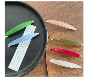 Detail of colorful acetate hair clips with gold metal base and engraved logo on dark tray