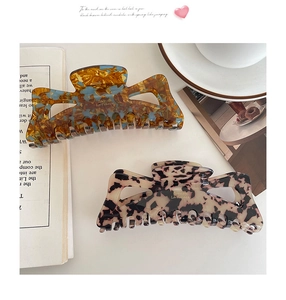 Close-up of large acetate claw clips with French golden text on marble background