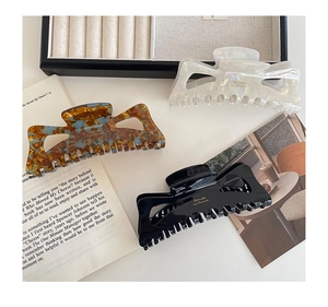 Three acetate hair claws in pearl, tortoise, and black colors with gold Barrette lettering