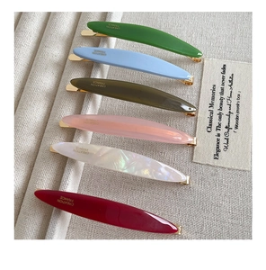 Close-up of six colorful acetate hair clips with gold metal base on canvas background