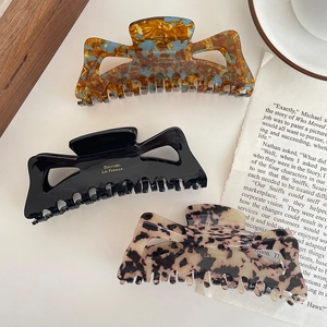 Three large acetate hair claws in tortoise shell, black, and cream with gold accents