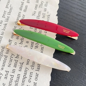 Three-piece set of elegant candy-colored acetate hair clips with gold lettering on a book