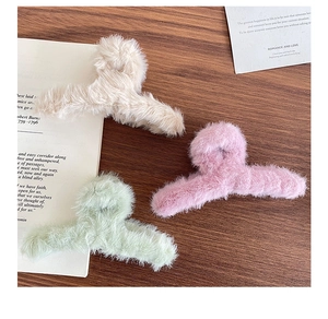 Vue détaillée de trois pinces à cheveux en peluche douce beige, rose et verte sur bois