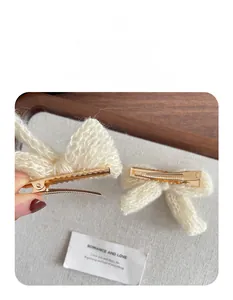 Detailed macro view of a white knitted bow hair clip with a golden metal alligator grip