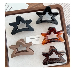 Close-up of five star-shaped claw clips in matte and glossy finishes on a wooden tray