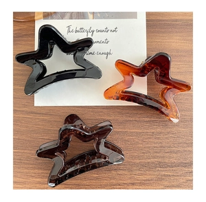 Detailed view of three matte star hair claws in black, amber, and coffee tones on wood