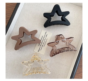 Set of four star-shaped matte and transparent claw clips displayed on a cream fabric tray