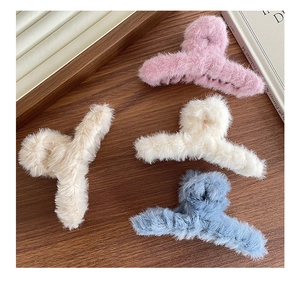 Détail de quatre pinces à cheveux en peluche rose, beige, bleu et kaki sur fond en bois