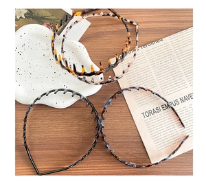 Three wave toothed headbands in black, tortoiseshell and floral patterns on wood