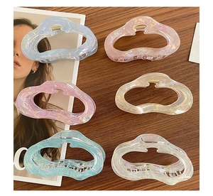 Flat lay of six colorful translucent hollow cloud hair claws on dark wood