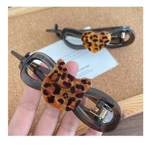 Detailed view of leopard print cat and heart shaped hair clips on a warm wooden base