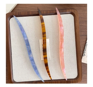 Detail of three curved acetate hair pins with marble patterns in blue, amber, and pink