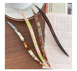 Detail of four acetate hair sticks with tortoise shell and marble patterns on a wooden desk