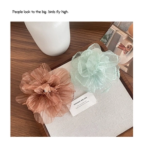 Nahaufnahme von rosa und mintgrünen Organza-Blumen-Haarspangen auf einem Holztablett mit Karte