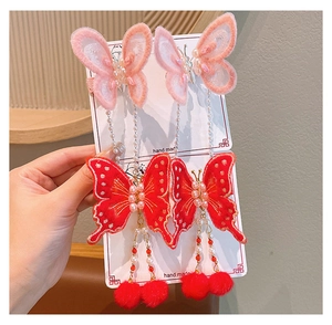 Détail d'une pince à cheveux papillon brodée à la main avec perles et pompons rouges