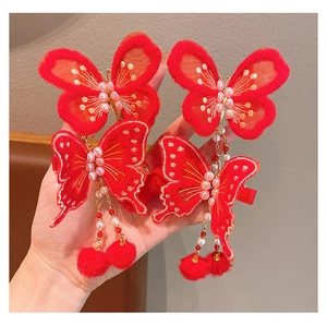 Détail de la pince à cheveux papillon rouge avec broderie, pompons et boules de poils