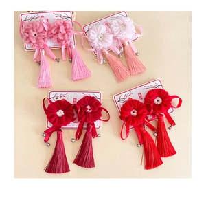 Détail de pinces à cheveux fleurs en feutre avec pompons en soie et clochettes décoratives