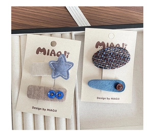 Close-up of cute blue fabric hair clips with star stitching and button details on display card