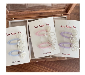 Detail of three pearl bow hair clips in light blue, pink, and purple on a display card