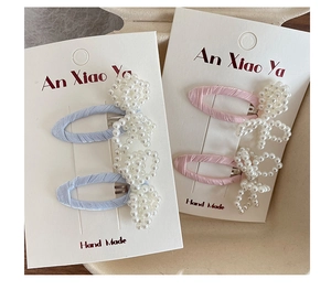 Detail view of handmade pearl bow hair clips in blue and pink on display card