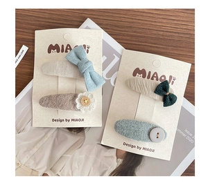 Detail of handmade fabric bow hair clips with embroidery and daisy accents on display card