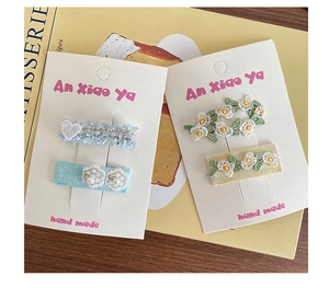 Détail de barrettes à fleurs et cœurs faites à la main avec broderies et perles sur cartonnettes