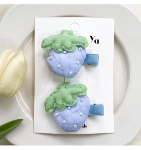 Détail de douces pinces à cheveux fraises en tissu bleu avec perles sur carte support