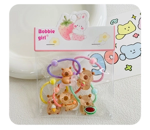 Detailed view of five colorful capybara hair ties with resin fruit charms in packaging