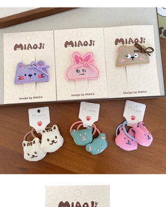 Detailed view of handmade embroidered animal hair clips and plush elastic ties on a desk