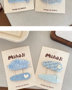 Detail of blue tweed hair clips with heart embroidery and lace bow on a beige card