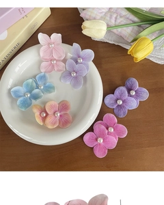 Detailed view of colorful fabric flower hair clips with pearl centers on a rustic table
