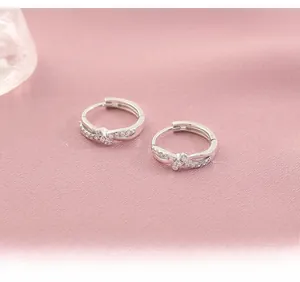 Close-up of silver twist hoop earrings with white zircon on pink silk fabric